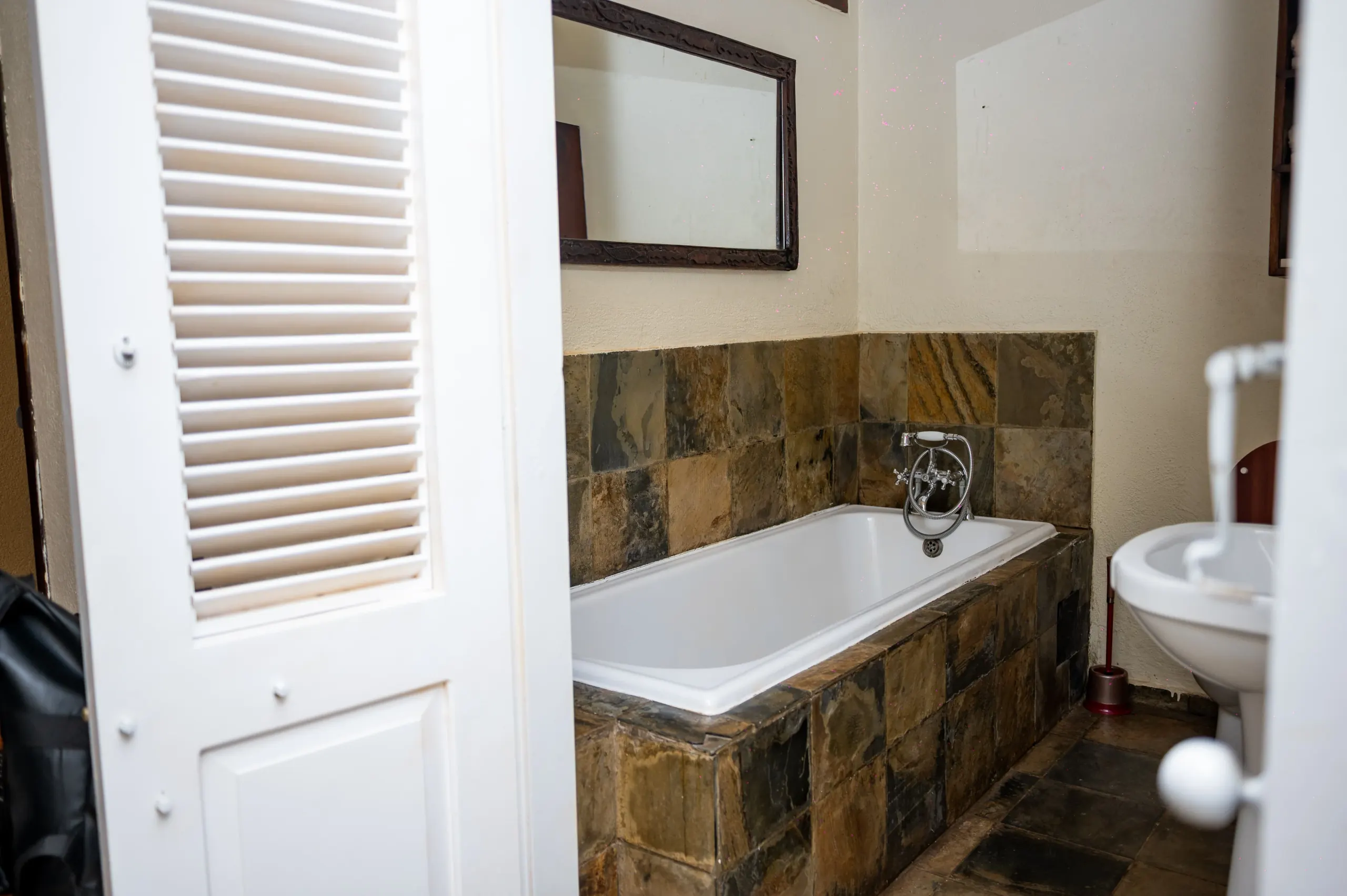 The bathroom of a Deluxe Room at The Emin Pasha Hotel & Spa, bath and basin against slate tiling