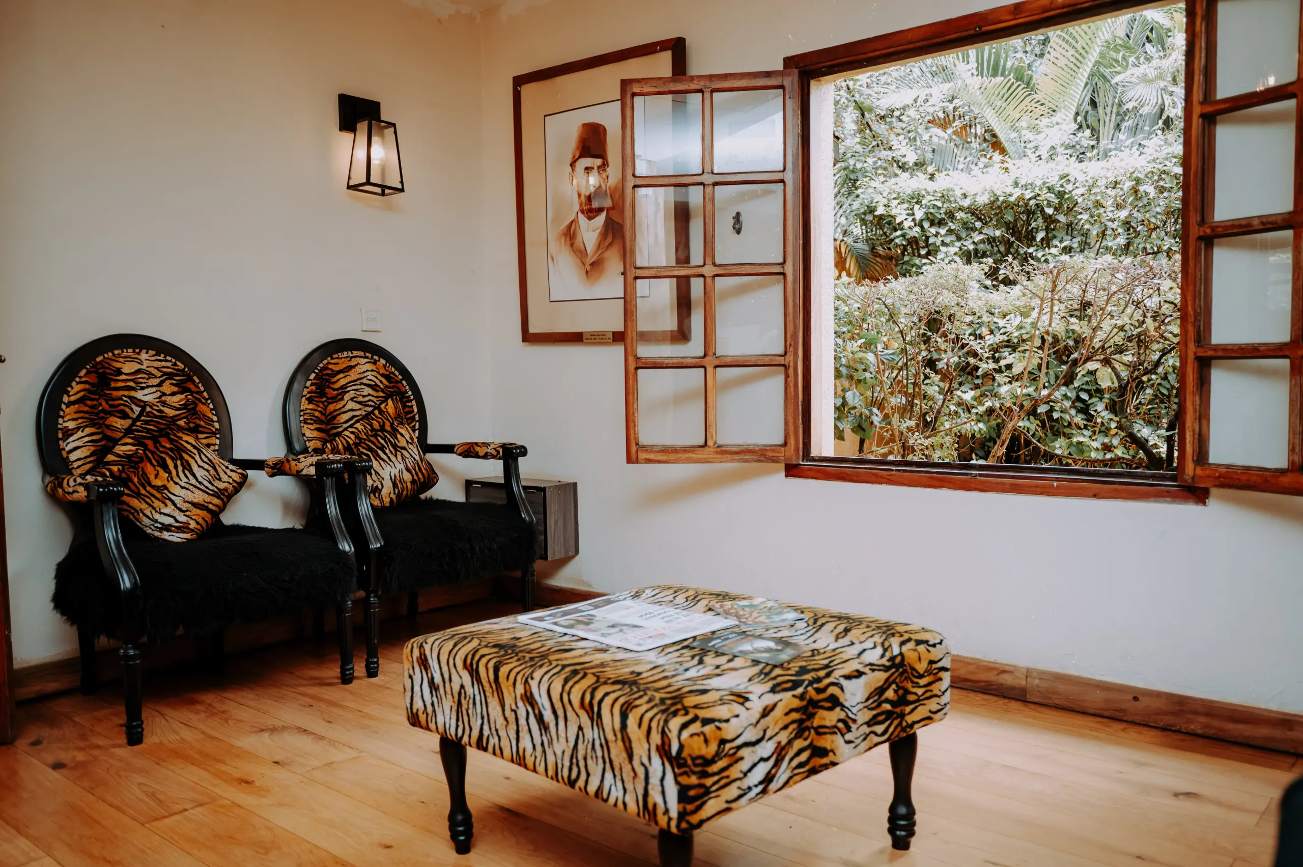 Patterned chairs beneath the Emin Pasha portrait, the window open to the garden