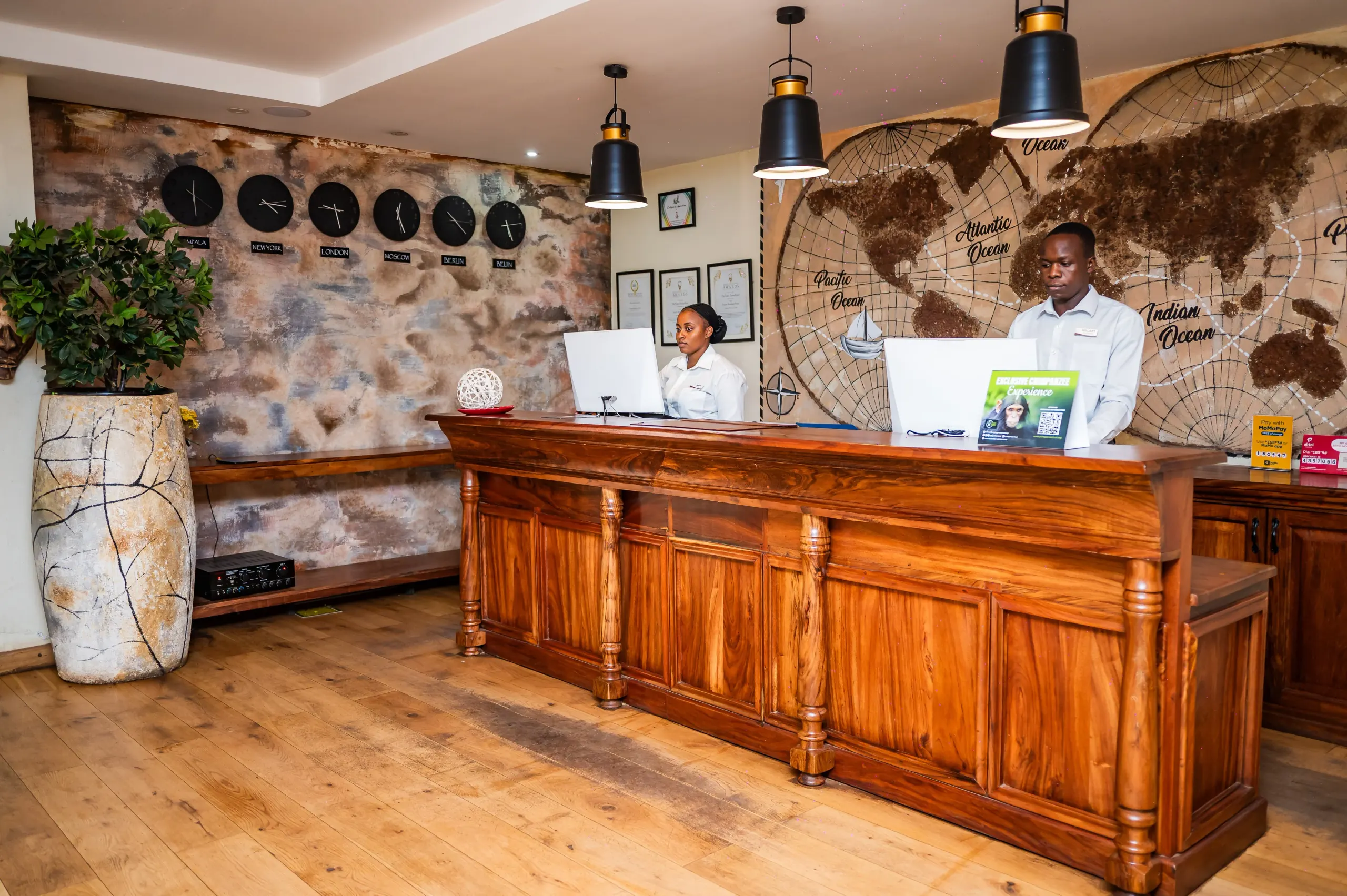 Two receptionists at the timber reception desk beneath a wall of world clocks