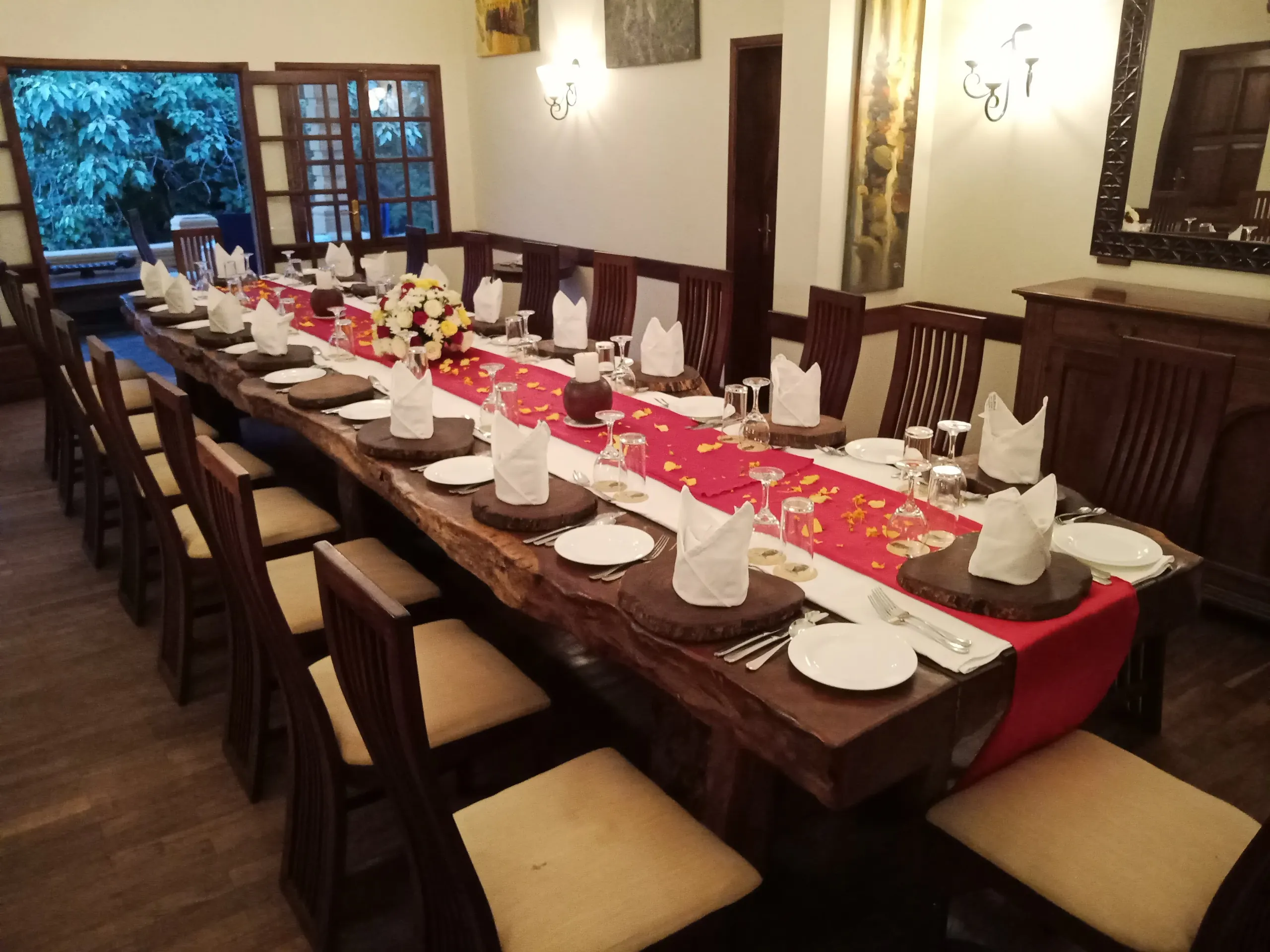 A long dinner table dressed with candles and flowers beneath trees