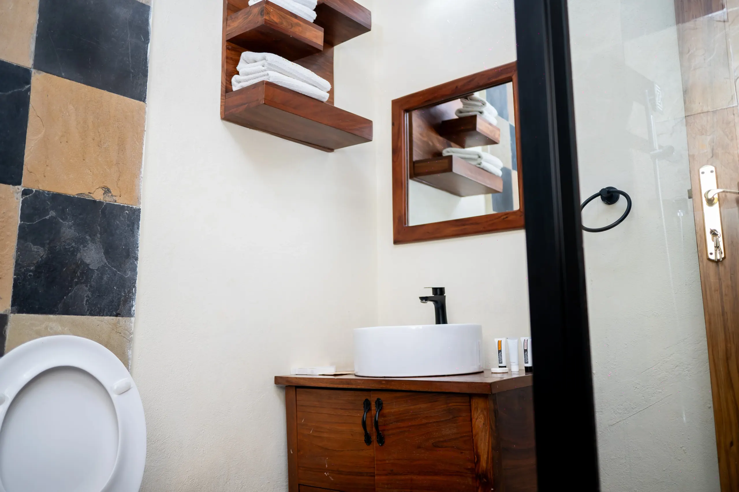 The bathroom of an Apartment Room at The Emin Pasha Hotel & Spa, with a basin, mirror and timber shelves